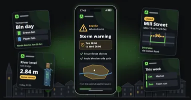 A phone showing a storm warning for the whole district with its time window and a map, surrounded by a city's routine posts, a bin day reminder, a river level, a road closure and the week's events, in front of a small town's rooftops.